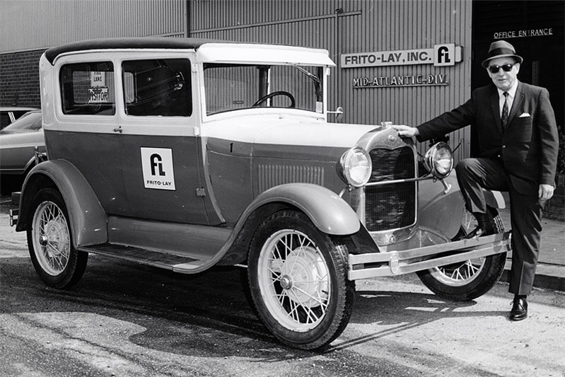 Man posing with an antique car with the Frito-Lay text written on it